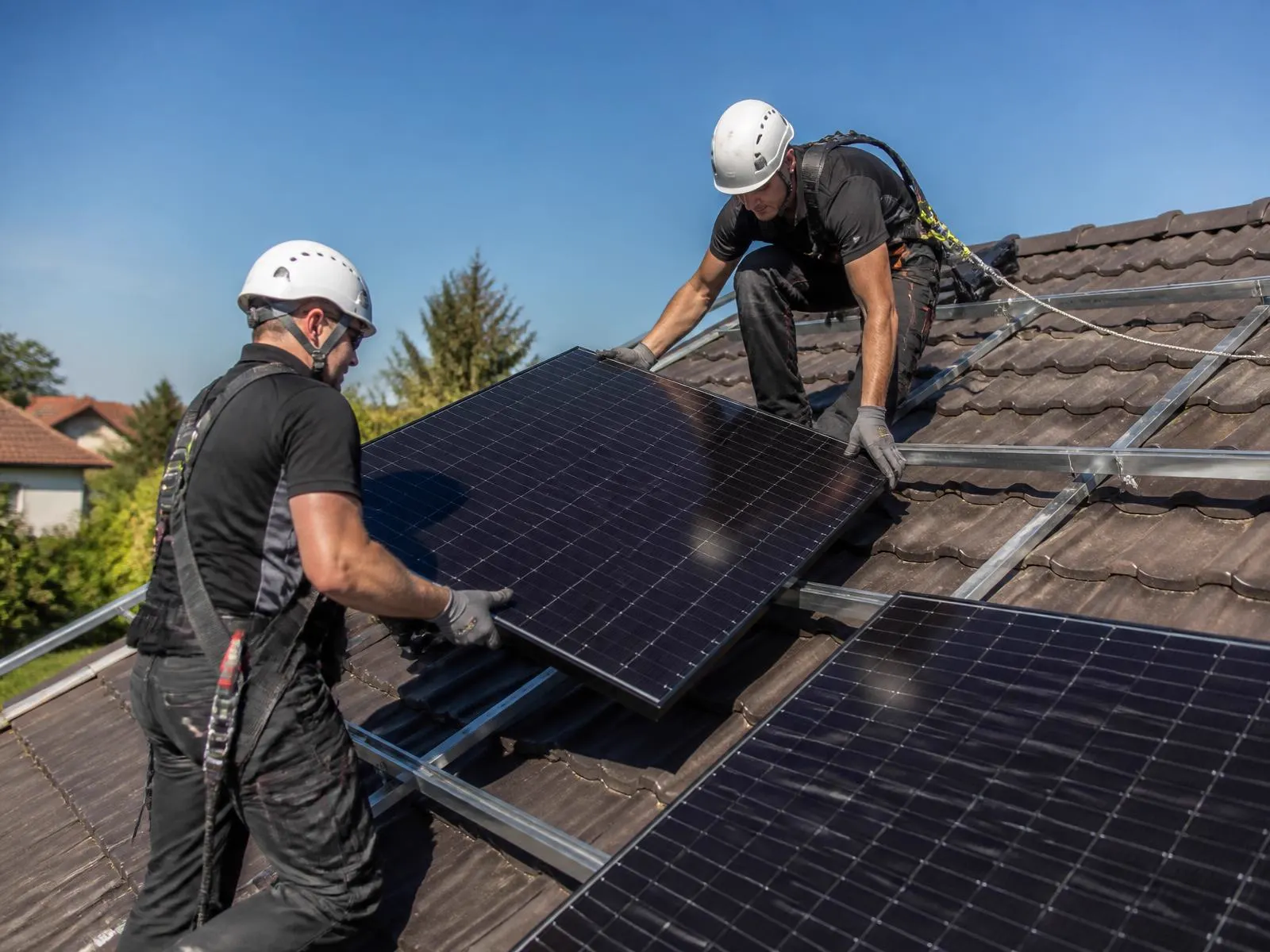 Dvaja montážnici v prilbách a s istením osádzajú fotovoltaický panel na hliníkovú konštrukciu