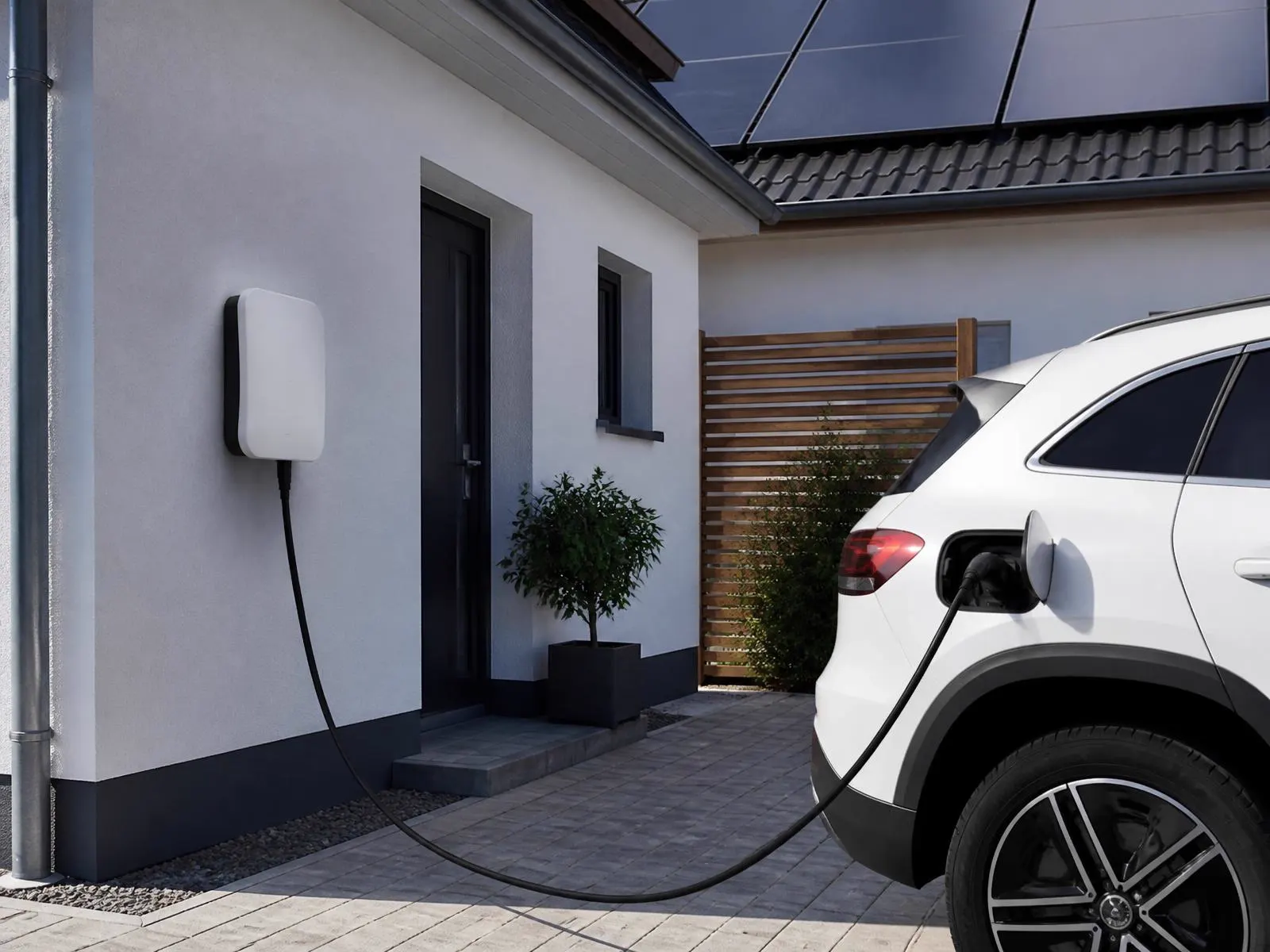 Nabíjacia stanica na fasáde domu s pripojeným elektromobilom a panelmi na streche